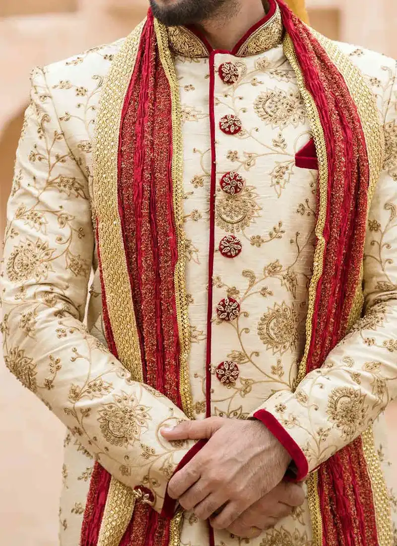 Close-up of ivory sherwani with intricate gold embroidery and red trim