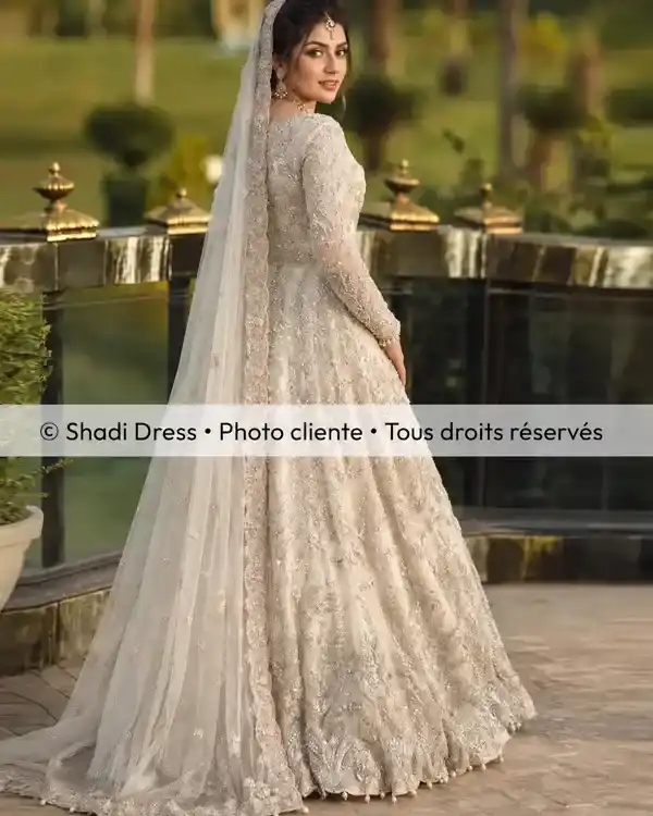 Mariée en robe ivoire brodée avec long voile assorti, photographiée dans un jardin