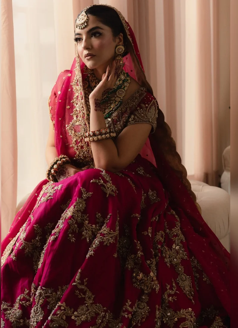 Full front view of fuchsia pink Pakistani baraat bridal lehenga choli featuring heavy gold zari embroidery, floral arches, a flared silk skirt and matching dupatta.
