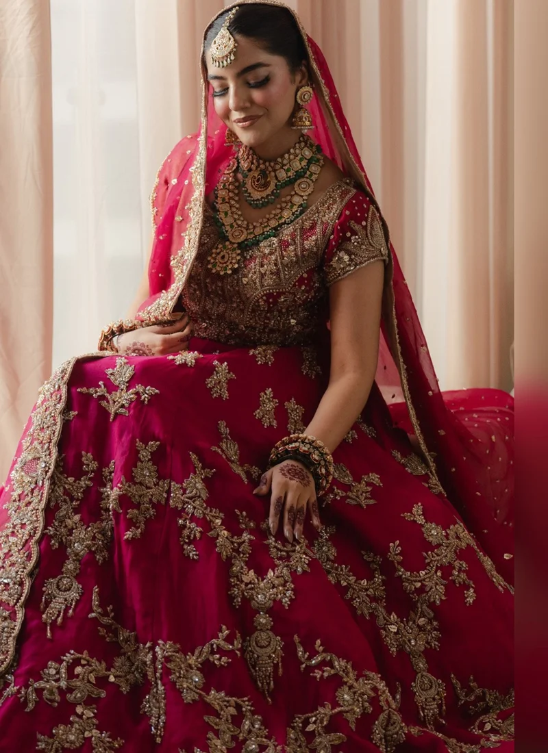 Fuchsia Pink Baraat Bridal Lehenga Choli with Gold Floral Embroidery – Front View Raspberry pink bridal lehenga choli with intricate gold dabka and tilla embroidery, cascading floral arch motifs, ornate hem border and sheer pink dupatta.