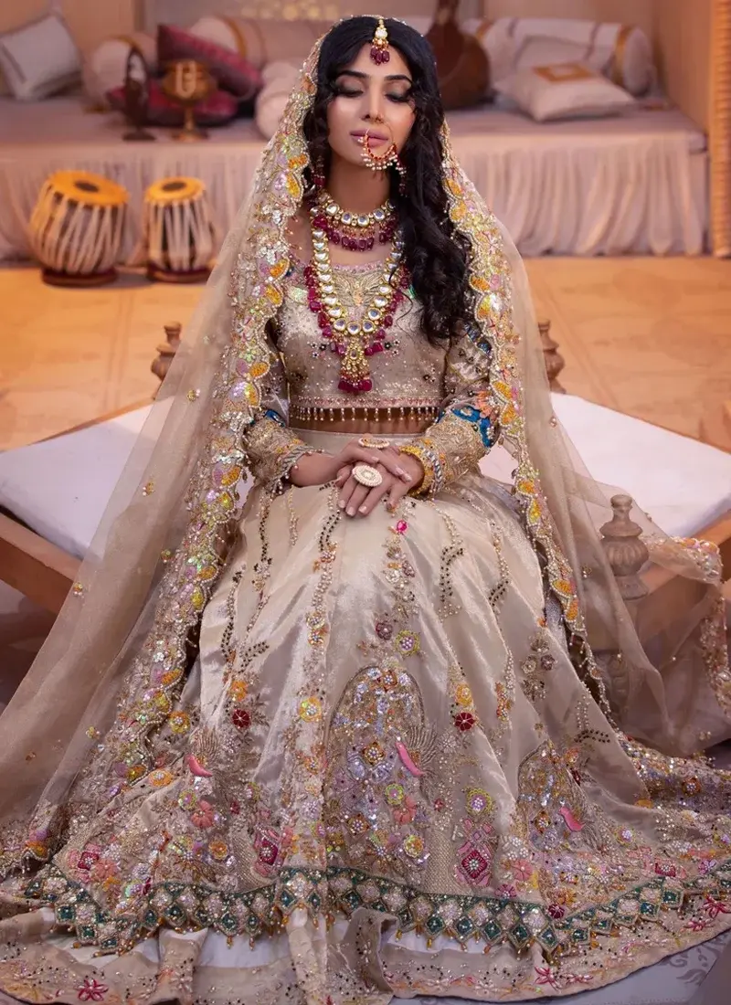 Champagne silk bridal choli close-up with gold neckline embroidery, pearl-drop edging and floral organza dupatta.