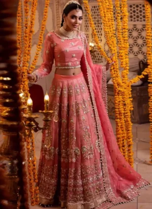 Coral pink bridal lehenga choli in three-quarter front view with gold floral embroidery and a wide ornate hem.