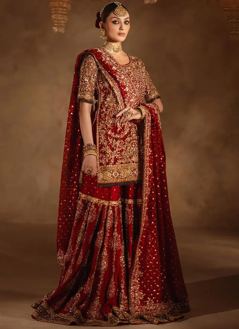 Deep red baraat gharara three-quarter view with a gold lattice shirt and flared embroidered legs.