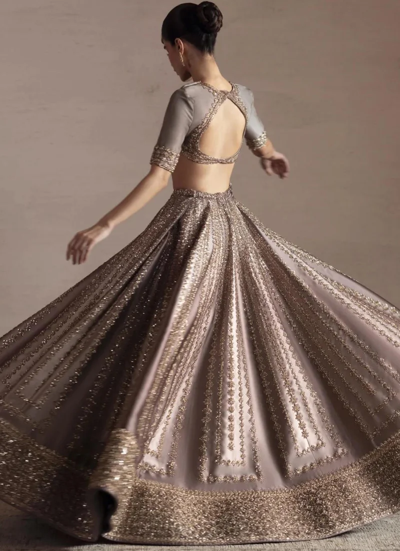 Taupe-grey bridal lehenga choli back view with a crossed keyhole opening and radiating gold floral embroidery.