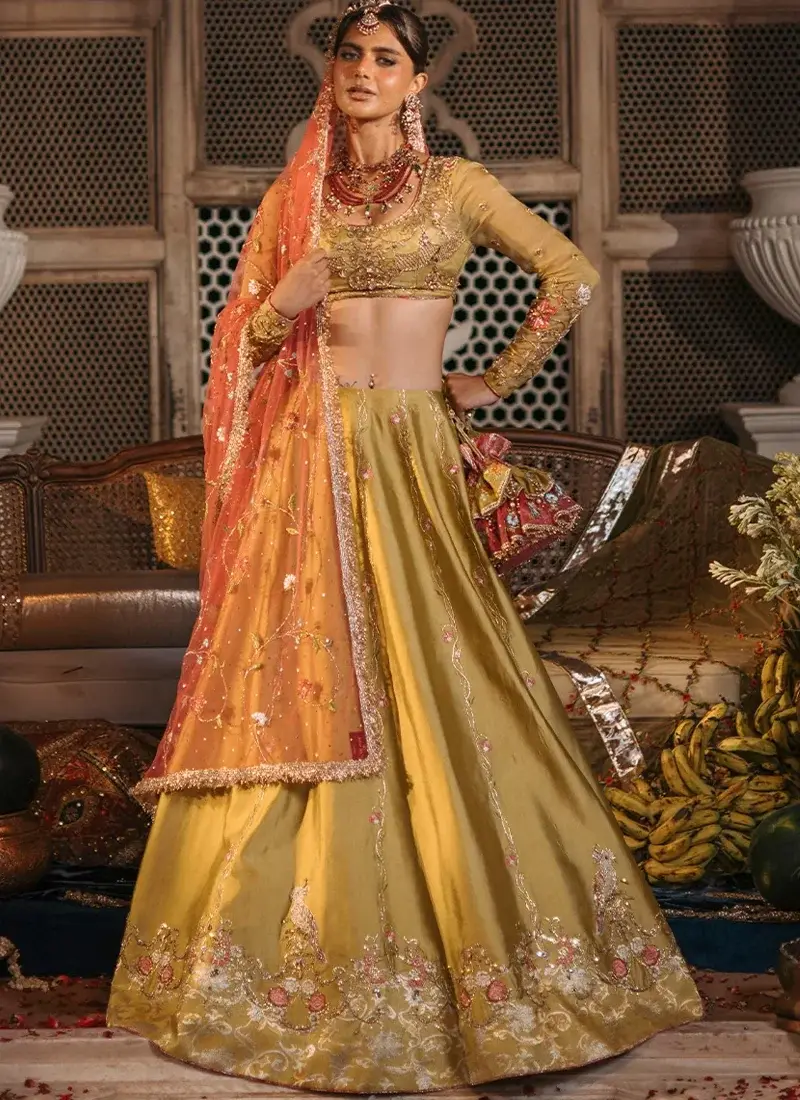 Mustard Mehndi Lehenga Choli with Kiran-Lace Dupatta Borders Mustard mehndi lehenga choli front view with coral dupatta and ornate gold floral hem embroidery