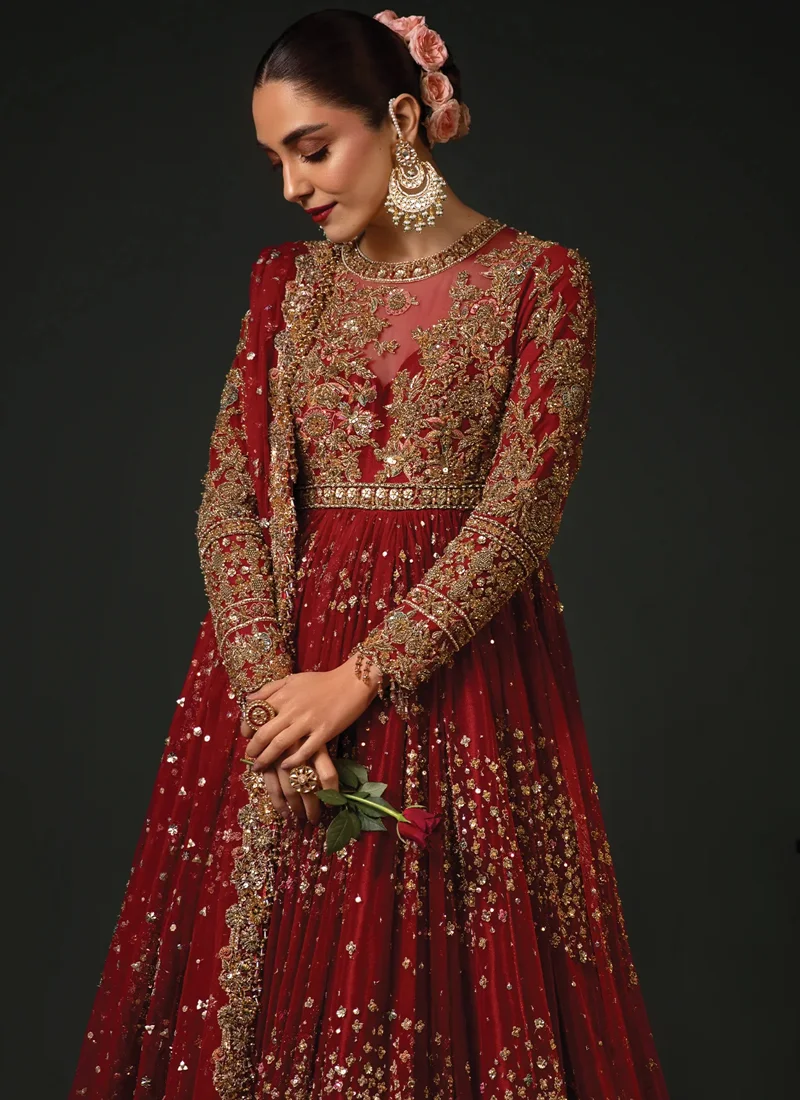 Red bridal pishwas side view with gold embroidered sleeves and cascading embellishments across the flared skirt
